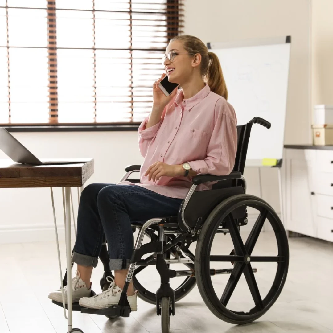 Woman in wheelchair smiling while talking on phone and sitting in front of laptop