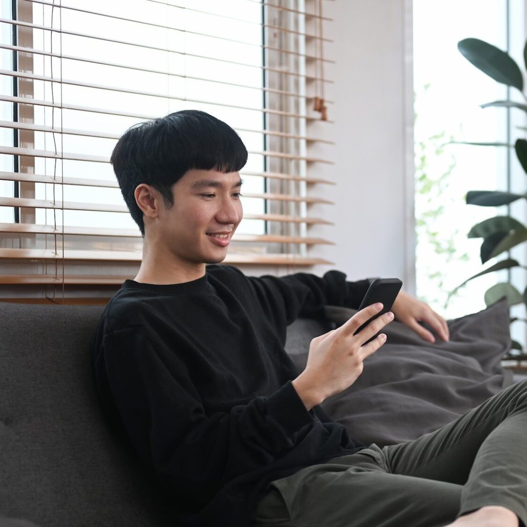 Man resting on couch and typing text message on mobile phone.
